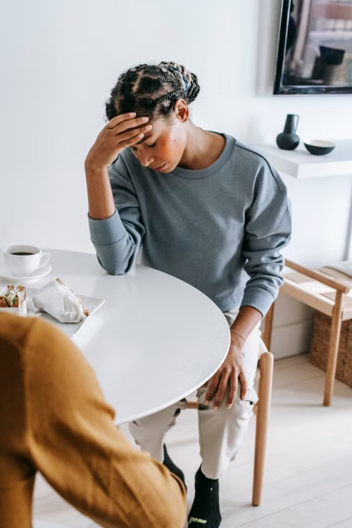 a woman sitting indoors and experiencing a headache
